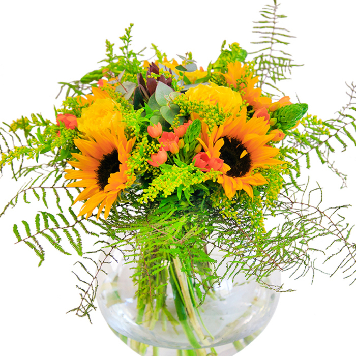 First impressions of this exquisite bouquet evoke pure, sun-warmed abundance-a showcase of Redbridge's natural beauty arranged in a clear, spherical vase. Sunflowers bold and bright, with velvety yellow petals and inky centres, beam outward, infusing the composition with a lively, welcoming light reminiscent of afternoons spent in South Park. Nestled between their golden faces are layers of pale yellow garden roses, forming intricate, spiral patterns with their softly textured petals-a nod to refined local elegance. Brilliant red clusters of Hypericum berries glisten among the foliage, creating sparkling highlights that bring contrast and vibrancy akin to the bustling atmosphere found at Redbridge's community events. Long, delicate fronds of fern and breezy sprays of filler add volume and movement, cascading gracefully to mimic the untamed greenery of nearby nature reserves. Hints of bluish-green eucalyptus peer through, elevating the bouquet with gentle coolness, while slender, upright spikes of green complete the ensemble's natural rhythm. The vase's transparency magnifies every verdant stem, underscoring the bouquet's structural grace within its pristine container. Subtle natural light enhances every detail, transforming this bouquet into an ideal centrepiece for birthdays or as a celebratory gesture-one that truly reflects the happiness at the heart of Redbridge gatherings.